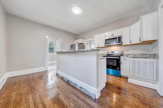 kitchen with dark hardwood / wood-style floors, a center island, light stone countertops, appliances with stainless steel finishes, and white cabinets