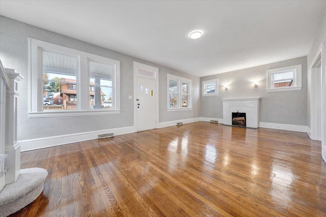 unfurnished living room with a brick fireplace, plenty of natural light, and hardwood / wood-style flooring