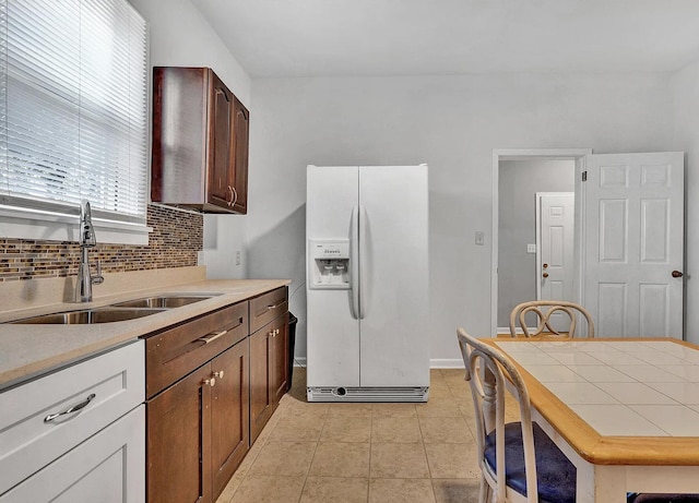 kitchen with sink, white fridge with ice dispenser, tasteful backsplash, dark brown cabinets, and light tile patterned flooring