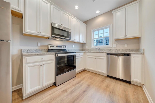 kitchen with white cabinets, appliances with stainless steel finishes, light hardwood / wood-style floors, and light stone countertops