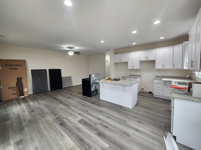 kitchen with light stone countertops, a center island, ceiling fan, white cabinets, and light wood-type flooring