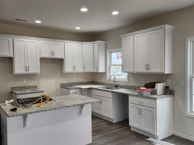 kitchen featuring light stone counters, a breakfast bar, sink, dark hardwood / wood-style floors, and white cabinetry