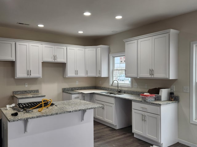 kitchen with white cabinetry, sink, light stone counters, dark hardwood / wood-style floors, and a breakfast bar