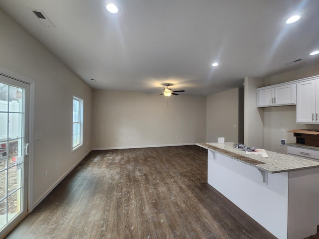 kitchen featuring a breakfast bar, dark wood-type flooring, ceiling fan, light stone countertops, and white cabinetry