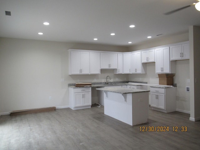 kitchen with light stone counters, a breakfast bar, white cabinetry, light wood-type flooring, and a center island