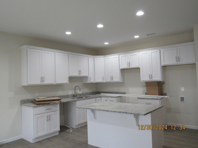 kitchen with a sink, a center island, light stone countertops, and white cabinets