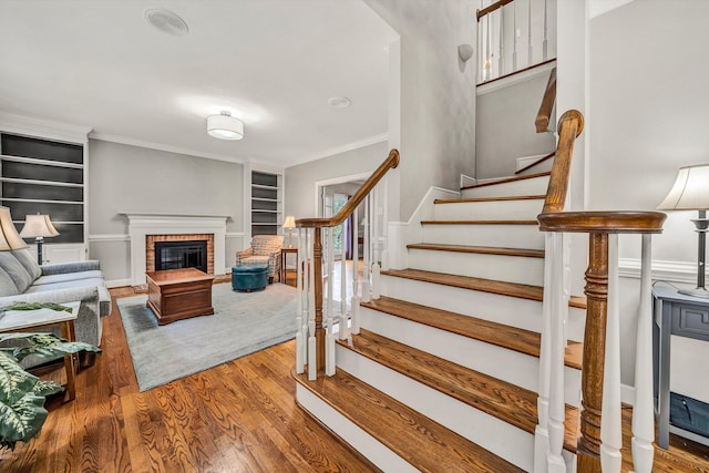 staircase with crown molding, built in features, wood-type flooring, and a brick fireplace