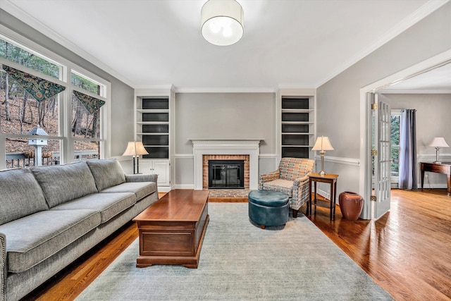 living room featuring wood-type flooring, built in features, a wealth of natural light, and a brick fireplace