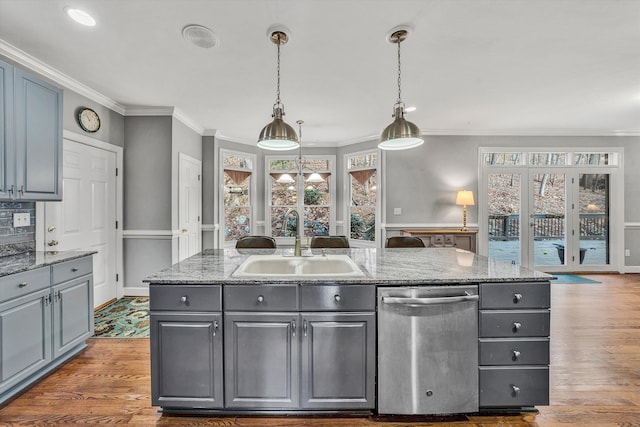 kitchen featuring a center island with sink, hanging light fixtures, sink, stainless steel dishwasher, and hardwood / wood-style flooring