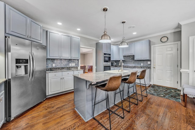 kitchen with decorative backsplash, appliances with stainless steel finishes, a kitchen island with sink, and gray cabinetry