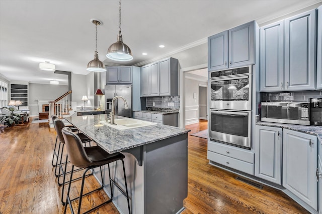 kitchen featuring light stone countertops, sink, tasteful backsplash, a kitchen island with sink, and appliances with stainless steel finishes