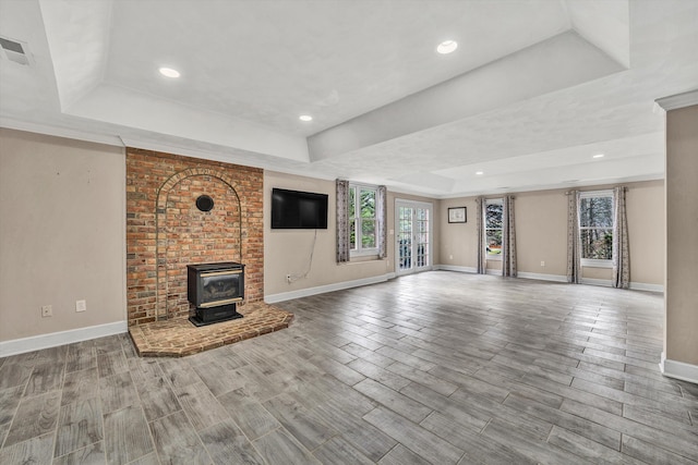 unfurnished living room featuring a wood stove and a tray ceiling