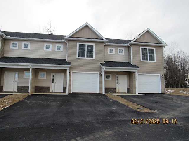 multi unit property featuring a garage, stone siding, driveway, and a shingled roof