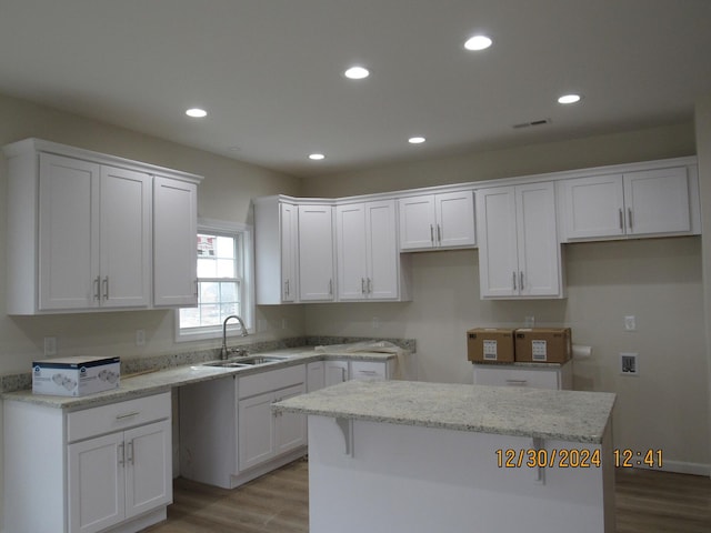 kitchen with recessed lighting, a kitchen island, a sink, white cabinetry, and light wood finished floors