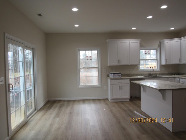 kitchen with white cabinets, sink, light stone countertops, light wood-type flooring, and a breakfast bar area