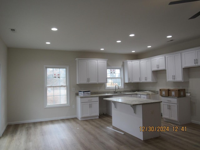 kitchen with white cabinetry, a kitchen island, light wood finished floors, and a sink