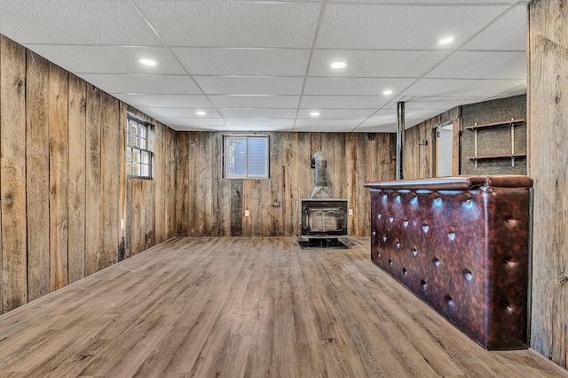 basement featuring hardwood / wood-style flooring, wood walls, and a wood stove