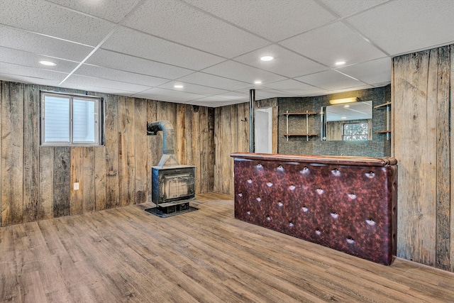 bar with a wood stove, a healthy amount of sunlight, a drop ceiling, and wood-type flooring