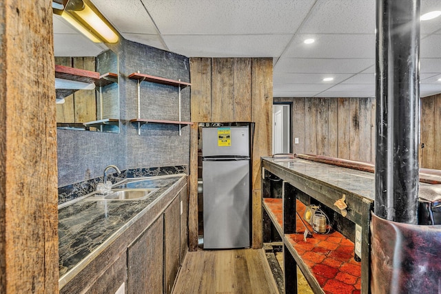 kitchen featuring a paneled ceiling, sink, wooden walls, hardwood / wood-style flooring, and stainless steel refrigerator