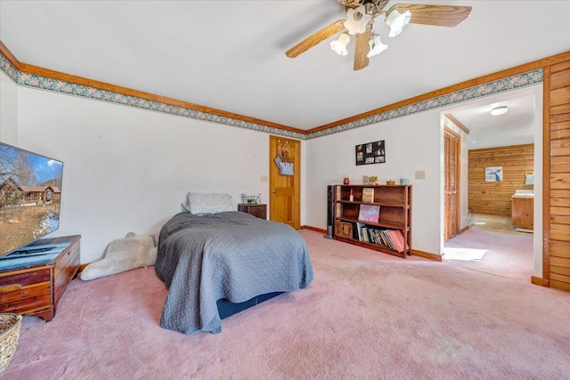 bedroom with wooden walls, carpet flooring, ornamental molding, ceiling fan, and ensuite bath