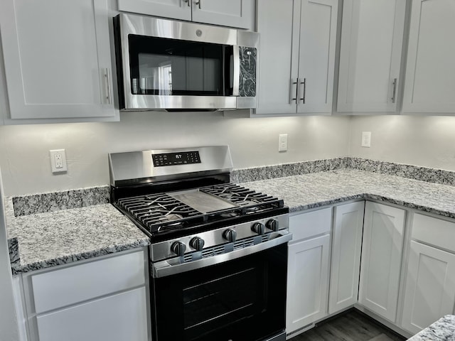 kitchen featuring appliances with stainless steel finishes, dark hardwood / wood-style flooring, light stone counters, and white cabinets