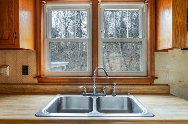 kitchen with light countertops, brown cabinets, a sink, and wallpapered walls