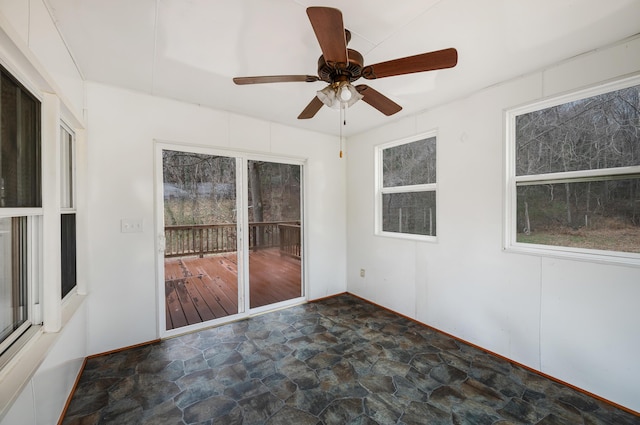 unfurnished room with stone finish floor, a ceiling fan, and baseboards