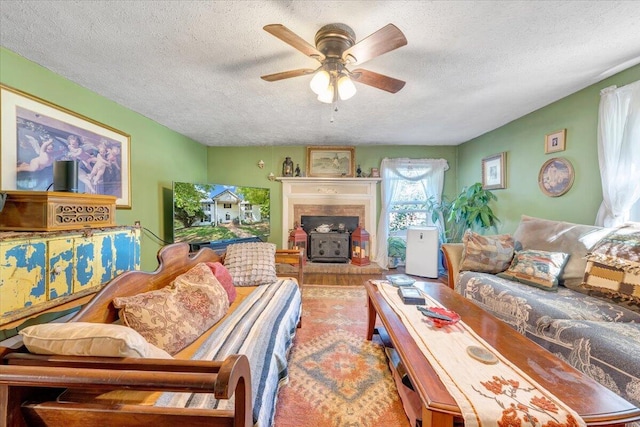 living room featuring ceiling fan, a wood stove, and a textured ceiling