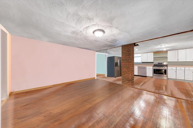 unfurnished living room with light hardwood / wood-style flooring, a textured ceiling, and decorative columns