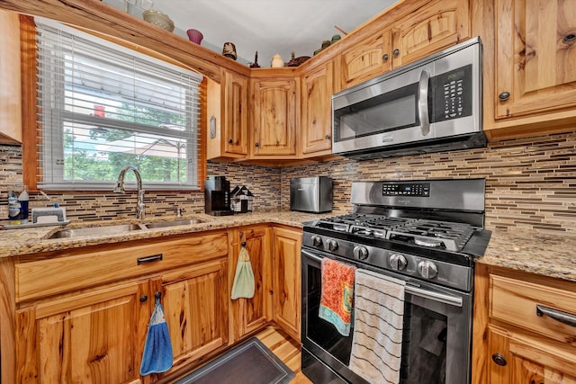 kitchen featuring decorative backsplash, light stone counters, sink, and appliances with stainless steel finishes