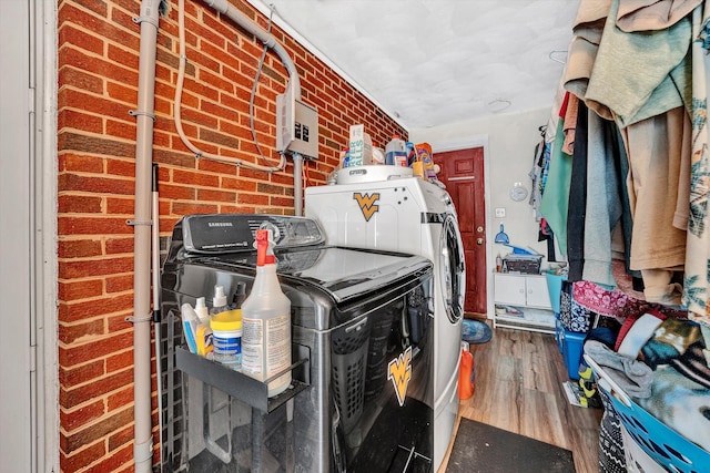 laundry area with hardwood / wood-style floors, washer and dryer, and brick wall