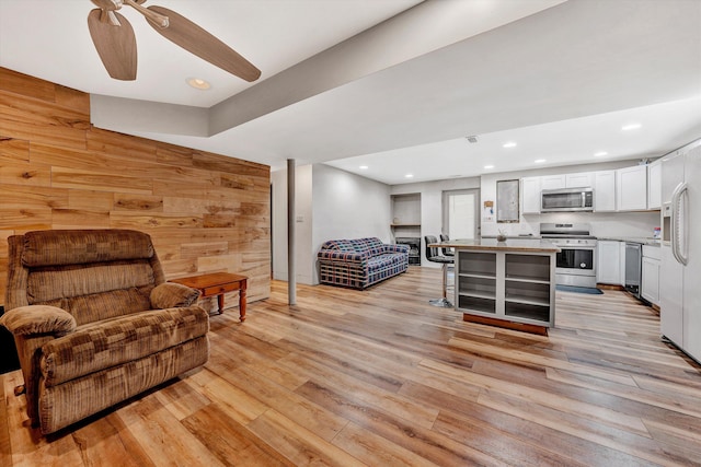 living room featuring light hardwood / wood-style floors, ceiling fan, and wood walls