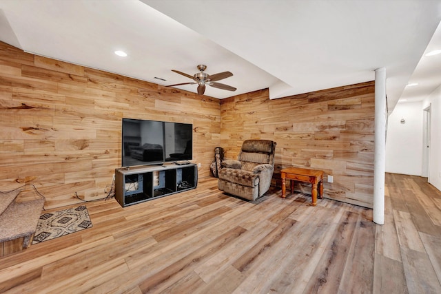 living room featuring light wood-type flooring, ceiling fan, and wood walls