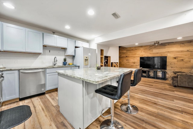 kitchen featuring ceiling fan, white refrigerator with ice dispenser, dishwasher, a center island, and wood walls