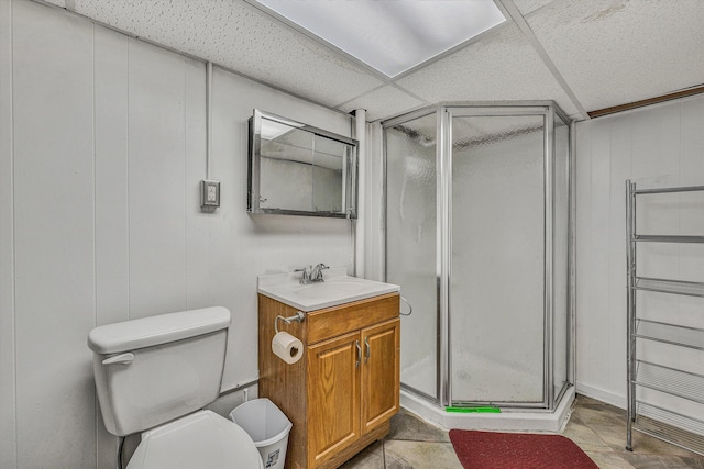 bathroom featuring a drop ceiling, vanity, a shower with door, and toilet