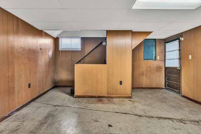 basement featuring electric panel, wooden walls, and a drop ceiling