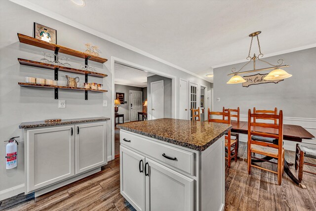 kitchen with dark stone counters, pendant lighting, crown molding, and dark wood-style floors