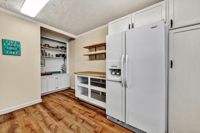 kitchen with wood finished floors, white refrigerator with ice dispenser, open shelves, ornamental molding, and a textured ceiling