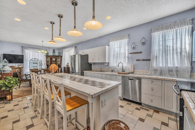 kitchen featuring tile counters, decorative light fixtures, a kitchen island, white cabinets, and appliances with stainless steel finishes