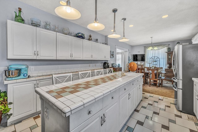 kitchen featuring a center island, stainless steel fridge, tile countertops, pendant lighting, and white cabinetry