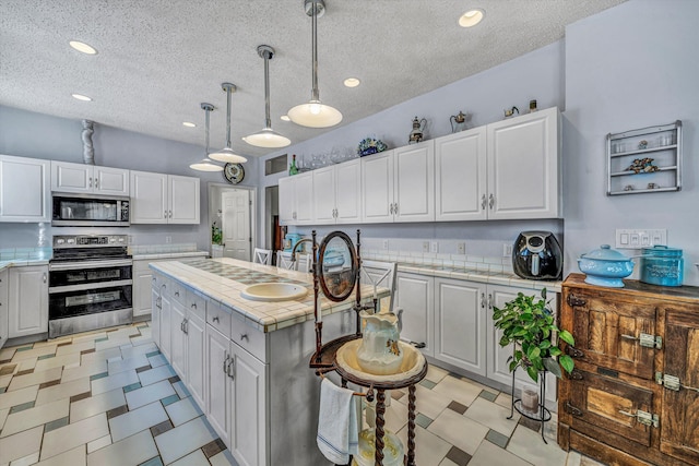 kitchen with white cabinets, stainless steel appliances, decorative light fixtures, and a kitchen island with sink