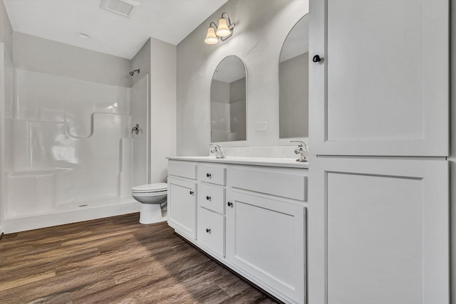 bathroom featuring a shower, double vanity, visible vents, toilet, and wood finished floors