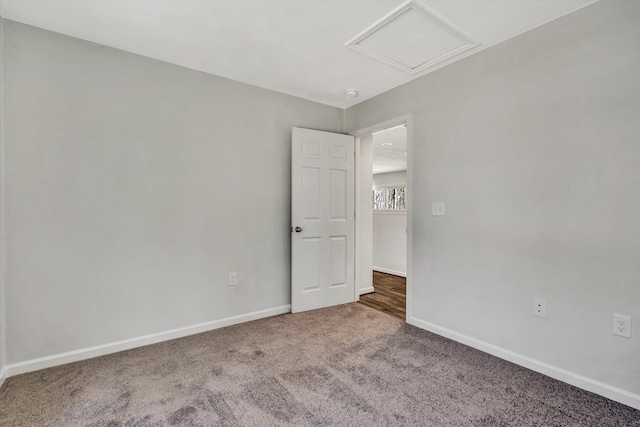 carpeted empty room with attic access and baseboards