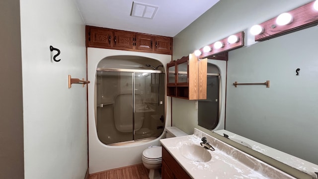 full bathroom with hardwood / wood-style floors, vanity, toilet, and bath / shower combo with glass door