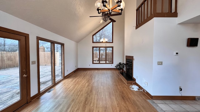 unfurnished living room with hardwood / wood-style floors, ceiling fan with notable chandelier, and high vaulted ceiling