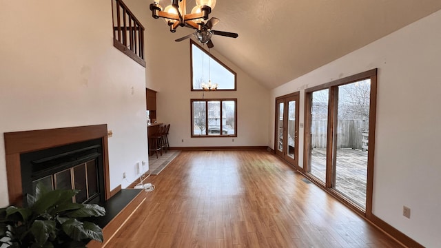 unfurnished living room featuring a towering ceiling, ceiling fan with notable chandelier, and hardwood / wood-style flooring