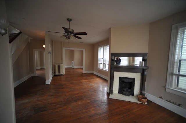 unfurnished living room featuring radiator, ceiling fan, dark hardwood / wood-style flooring, and a stone fireplace