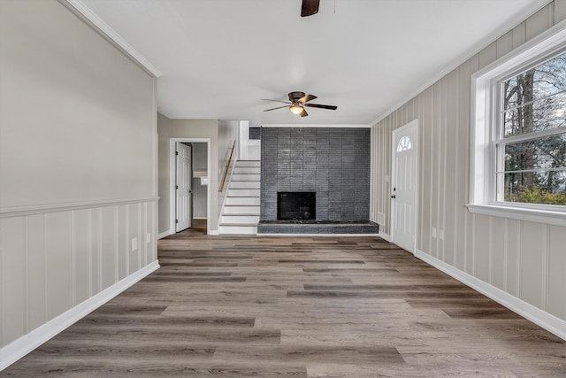 unfurnished living room with ceiling fan, a large fireplace, wood-type flooring, and ornamental molding