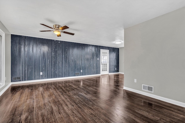 empty room featuring wood-type flooring, ceiling fan, and wooden walls