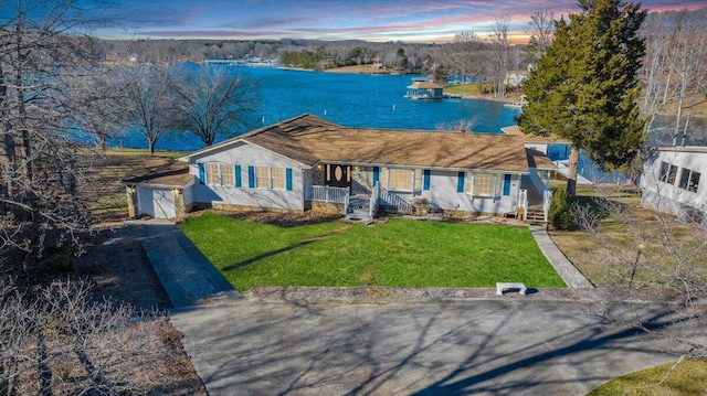 ranch-style home featuring a porch, a lawn, a garage, an outdoor structure, and a water view